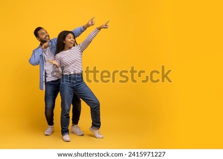 Check This. Happy black couple pointing aside at copy space on yellow background, young african american man and woman recommending something, showing free place for your design or advertisement Royalty-Free Stock Photo #2415971227