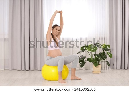 Pregnant woman doing exercises on fitness ball in room. Home yoga
