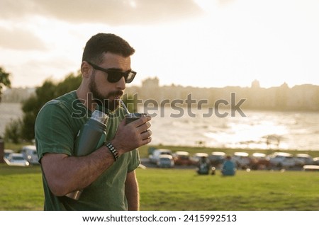 Man drinking chimarrao, mate (an infusion of yerba mate with hot water) at sunset in uruguay Royalty-Free Stock Photo #2415992513