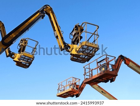 Two aerial working platforms of cherry pickers in front of other two. Blue sky background. Royalty-Free Stock Photo #2415993937