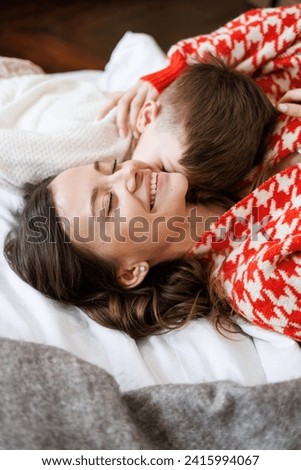 Toddler boy in sweater kissing happy mother on bed Royalty-Free Stock Photo #2415994067