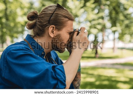 Young man in casual clothing photographing the view while standing at the city park outdoors. Caucasian hipster photographer taking shots of city views, walking around in town