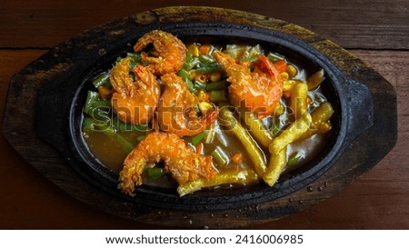 landscape closeup picture of Crispy Shrimp Steak on the hot plate with French fries and vegetables. This delicious shrimp steak is served with barbeque sauce on a hot plate on a wooden board