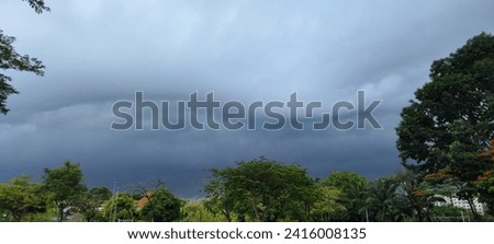 The image shows a dark, stormy sky. The clouds are thick and ominous, and the trees are silhouetted against the sky. The scene is one of foreboding and danger.
