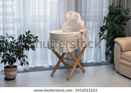 Empty white Moses basket on a wooden stand in a sunny room.