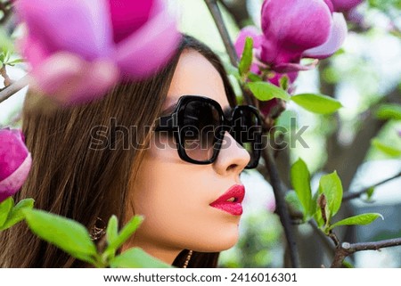 Young woman near blossom park. Spring girl. Woman on spring blooming tree. Beautiful young woman in summer style outfit with flowers outdoor. Spring sunshine park. Beauty woman enjoying smell in a