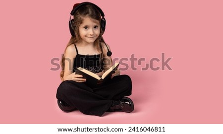 The picture of a very cute little girl posing while she was reading a very interesting book and she has a pair of headphones on her head through which she listens to music and is focused on the book
