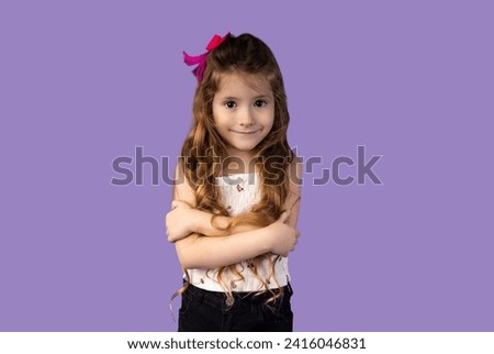 A very, very beautiful little girl with an infectious and attractive smile, the girl has blond hair and brown eyes, her hair is wavy made by her mother at home, she is pictured on a purple background.