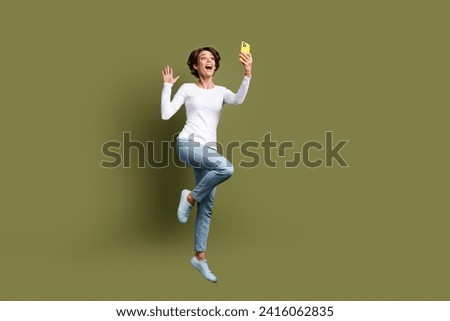Full size photo of attractive young woman jumping video call palm wave dressed stylish white clothes isolated on khaki color background