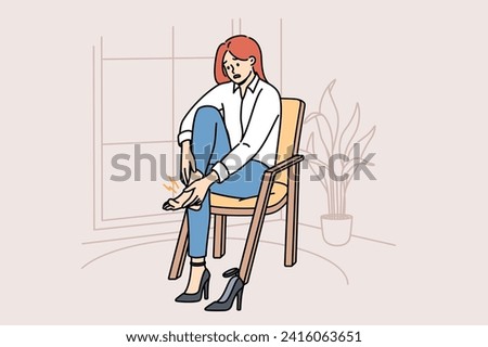 Woman with varicose veins feels pain in legs due to uncomfortable high-heeled shoes, sits on chair in apartment. Girl needs medicinal ointment to cure varicose veins or calluses on heel Royalty-Free Stock Photo #2416063651