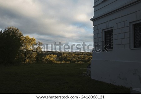 From the corner of the building we can see the endless field, the river and the sky. The corner of the building against the background of the sky and the green cliff.