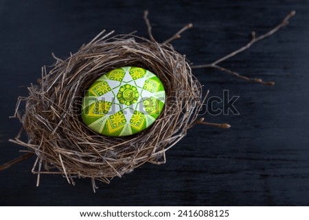 Traditional Ukrainian Easter egg in green and yellow colors in a bird's nest on a dark background Royalty-Free Stock Photo #2416088125