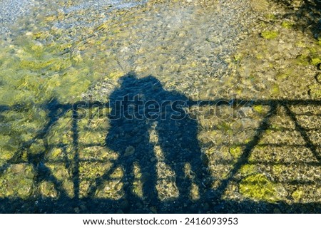 Silhouette of romantic view of two people shapes, man and woman shadow reflection on the Manitou River on bidge at Sandfield Dam, Lake Manitou.  Royalty-Free Stock Photo #2416093953