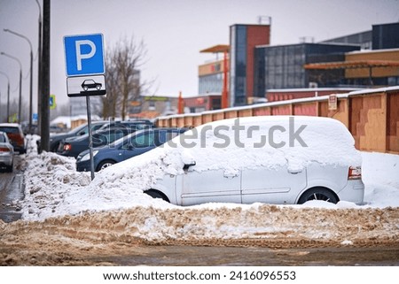 Parking sign allowing parking in the city and buried car under deep snow after blizzard. Parking sign, and car stucked in snow on background. Extreme winter weather. Selective focus