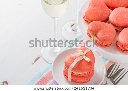 Heart shaped macaroons with ribbon on white plates with champagne on white wood background