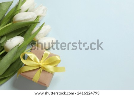 Beautiful white tulips and craft gift on colored background