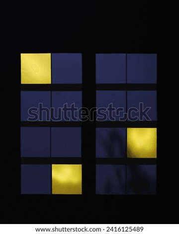 A modern building exterior at night, illuminated windows creating a pattern. Minimalistic creative abstract concept of city life, loneliness from paper stickers on a black background.