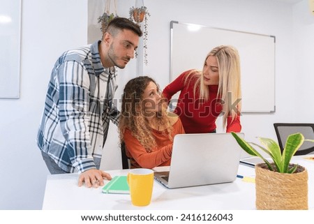 Three colleagues closely reviewing and discussing content on a laptop screen in a modern office environment Royalty-Free Stock Photo #2416126043