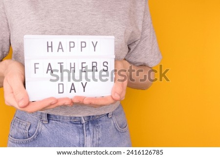 Happy Fathers Day. Woman hold in hands lightbox with letters in front of yellow background. 