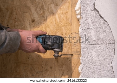 A skilled Craftsman demonstrates precision, making notches in a wooden frame on the wall using a multicutter during room renovation.