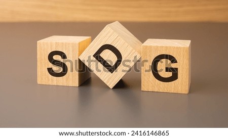 Wooden cubes with 'SDG' on brown background symbolize commitment to Sustainable Development Goals, fostering global efforts for a sustainable and inclusive future.