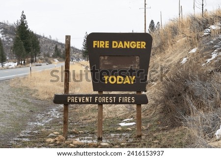 Blank "Fire Danger Today Prevent Forest Fires" sign in winter surrounded by patchy snow and wet conditions near road.    Royalty-Free Stock Photo #2416153937