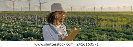 Female agronomist making notes in clipboard on cabbage field during harvesting. Agricultural concept