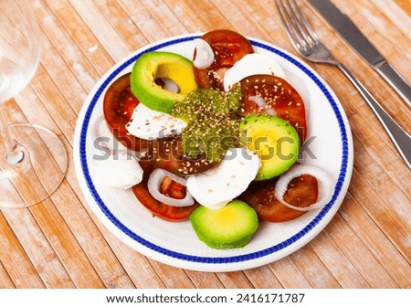 Delicious dietary Caprese salad, made from fresh chopped tomatoes, onions, avocado, mozzarella, sprinkled with sesame seeds ..and doused with Pesto sauce Royalty-Free Stock Photo #2416171787