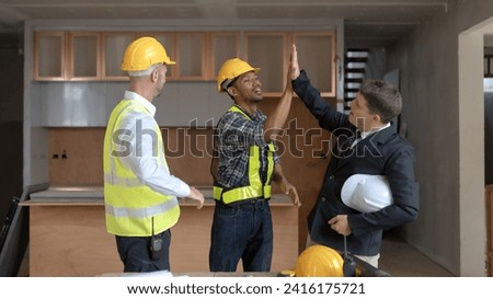 Three diverse professionals celebrate project progress inside a construction site with a high-five.