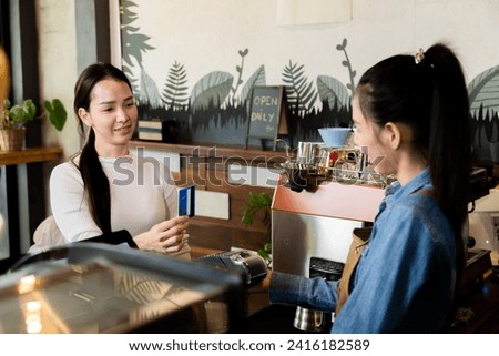 Asian waitress barista worker accepts credit card cashless payments from customer female in cafe restaurant, happy woman open bakery coffee shop, small business entrepreneur start-up lifestyle 
