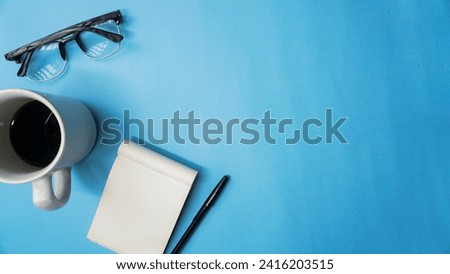 workspace desk with notebooks, pens, glasses, and coffee on blue background