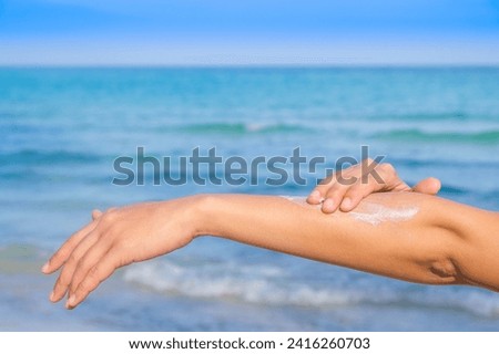Woman applying sunscreen and taking care of her skin to protect her skin from UV rays She applies sunscreen on her hands and arms. Very sunny sea background Health and skin concept Royalty-Free Stock Photo #2416260703
