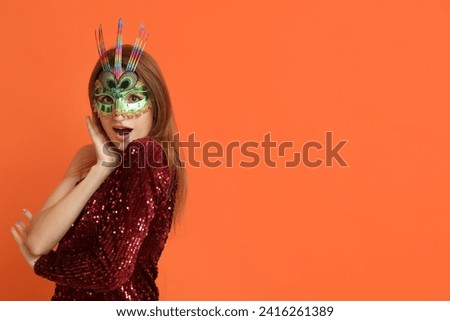Shocked young woman in carnival mask on orange background