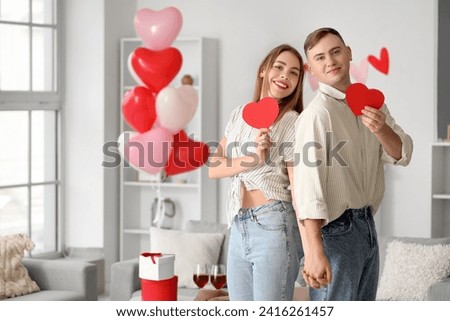 Beautiful young couple with paper hearts celebrating Valentine's Day at home