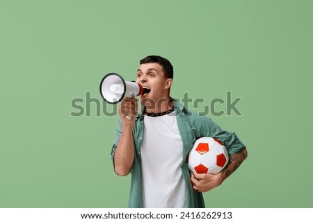 Young man with soccer ball and loudhailer on green background Royalty-Free Stock Photo #2416262913
