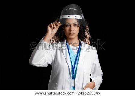 Female African-American medical intern in protective mask on black background
