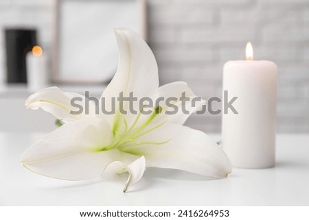Burning candle and beautiful lily flower on light table in room, closeup
