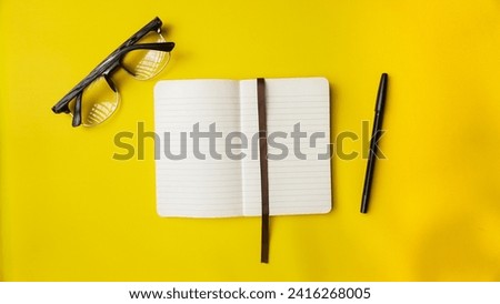 workspace desk with notebooks, pens, and glasses on blue background