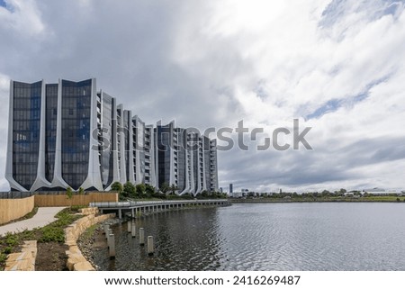 Modern architecture apartment buildings with a tulip design style on a curved waterfront shoreline on an artificial lake with overcast sky on the Gold Coast in Queensland, Australia. Royalty-Free Stock Photo #2416269487