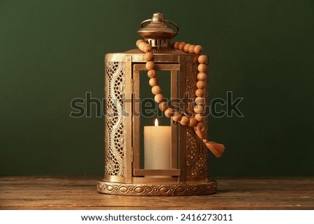 Muslim lamp with burning candle and prayer beads for Ramadan on wooden table against dark green background Royalty-Free Stock Photo #2416273011
