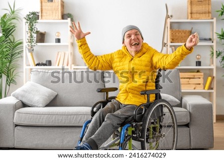 Happy and expressive disabled man in wheelchair raising hands in joy at home