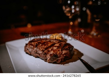  close-up of a grilled steak on a white plate with a side, in a restaurant with a bokeh background.