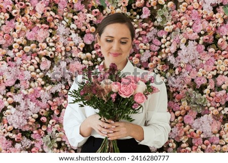 Cute healthy woman smiling and holding colorful pink color flower bouquet on floral spring or summer background, studio fashion beauty portrait