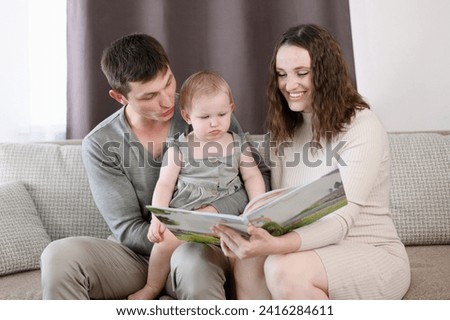 Parents read a book to their child, look at educational pictures, sitting on couch at home.Happy family concept,learning