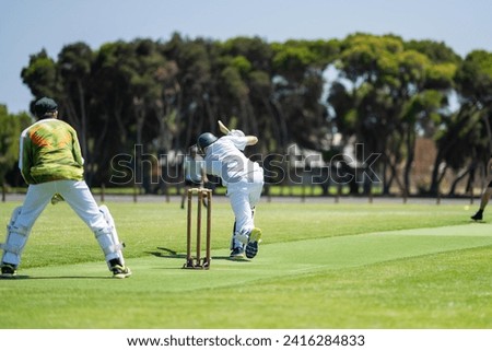 a local cricket match being played on a green cricket oval in summer in australia. australian cricketer batting and bowling in a game in summer