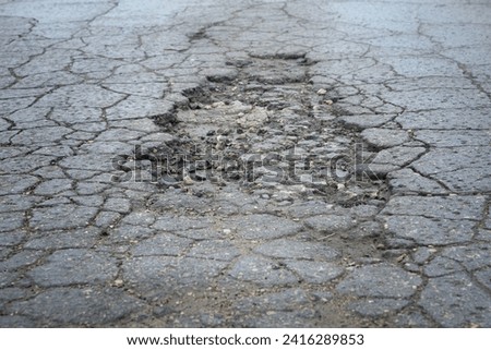 A large hole in the asphalt with cracks on the road. Close-up. Background. Space for text. Royalty-Free Stock Photo #2416289853