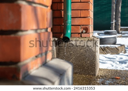 Photo of a downpipe in winter with leaking water and snow in the background.