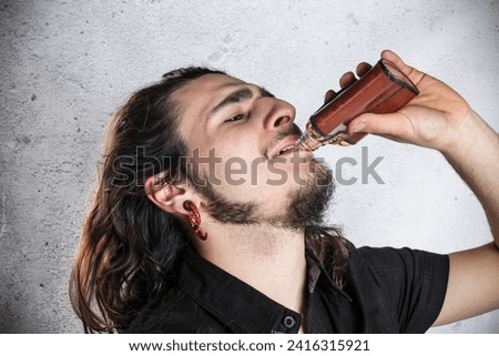 Young male sipping alchool from a hip flask Royalty-Free Stock Photo #2416315921