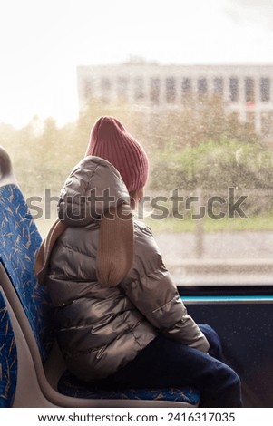 Rear view of child girl 5 year old riders on public bus metropolitan transport, looking at window. Kid girl in trolleybus, city travels lifestyle. Public urban transport concept. Copy ad text space Royalty-Free Stock Photo #2416317035