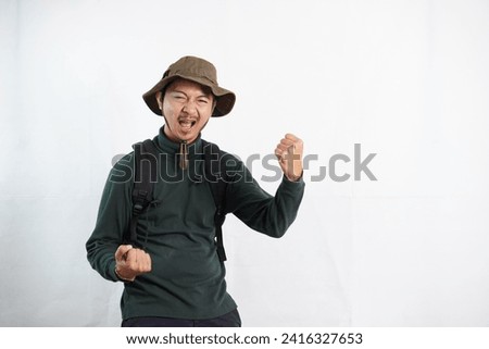 Young man wearing traveling hats and backpack standing over isolated white background very happy and excited doing winner gesture with arms raised, smiling and screaming for success. Celebration